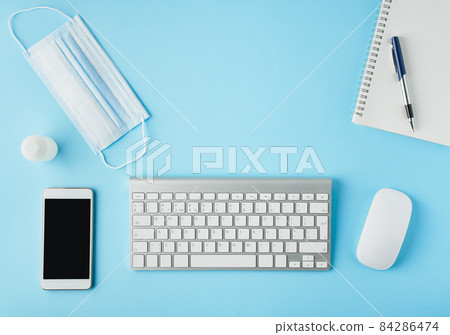 Bright blue modern desk with medicine mask and sanitizer. Top view. Social distance in office. 84286474