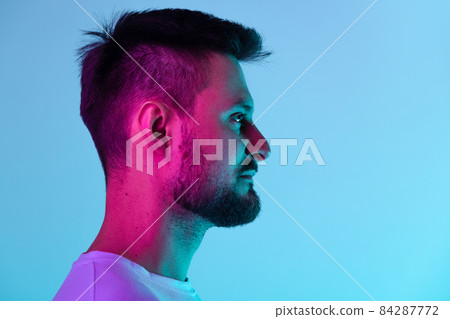 Close-up side view portrait of bearded man calmly looking away, posing isolated over blue background in neon light 84287772