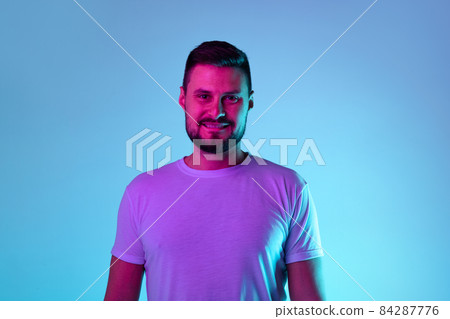 Cropped portrait of smiling cheerful man posing isolated over blue background in neon lights Cropped portrait of smiling cheerful man posing isolated over blue background in neon lights 84287776
