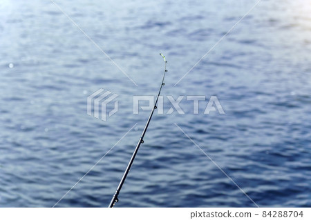 Fishing rod on a background of blue water, selective focus with copy space for text. Fishing rod on a background of blue water, selective focus with copy space for text. 84288704
