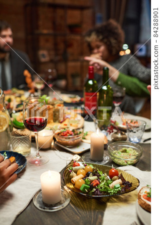 Close-up of dining table with delicious dishes and glasses of red wine with people sitting in the background 84288901