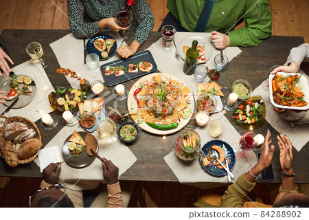 High angle view of dining table with delicious dish and appetizers with people sitting at the table High angle view of dining table with delicious dish and appetizers with people sitting at the table 84288902