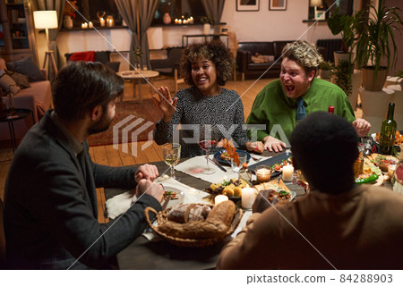 Group of friends talking to each other and laughing during dinner party in the living room Group of friends talking to each other and laughing during dinner party in the living room 84288903