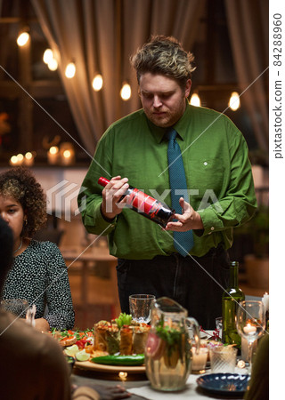 Man opening the bottle of red wine during a dinner with his family to say the celebratory toast 84288960