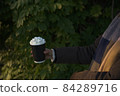 Young women in winter coat and scarf holds a takeaway beverage. Side on 84289716