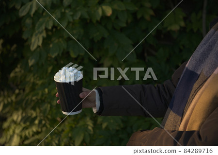 Young women in winter coat and scarf holds a takeaway beverage. Side on Young women in winter coat and scarf holds a takeaway beverage. Side on 84289716