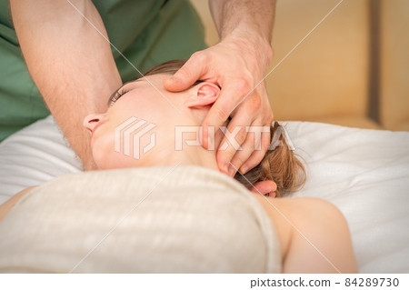 Osteopath doing massage on the female head in rehabilitation clinic center. Osteopath doing massage on the female head in rehabilitation clinic center. 84289730