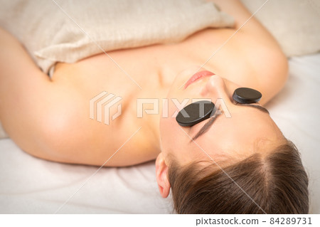 Massage with stones on the eyes of young woman getting a treatment in a beauty spa. Massage with stones on the eyes of young woman getting a treatment in a beauty spa. 84289731