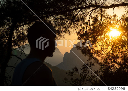 Silhouette of man in front of scenic view of mountains against sky during sunset,through trees . Silhouette of man in front of scenic view of mountains against sky during sunset,through trees . 84289996