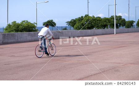 A handsome casual man is going to the office by bicycle. He is driving bike in front of office district. A handsome casual man is going to the office by bicycle. He is driving bike in front of office district. 84290143