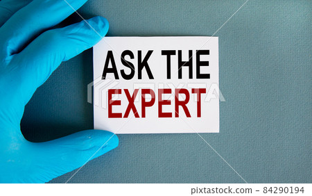 Hand in blue glove with white card. Concept words 'ASK THE EXPERT'. Medical concept. Hand in blue glove with white card. Concept words 'ASK THE EXPERT'. Medical concept. 84290194