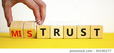 Mistrust or trust symbol. Businessman turns wooden cubes, changes words 'mistrust' to 'trust'. Beautiful yellow table, white background. Business and mistrust or trust concept, copy space. 84290277