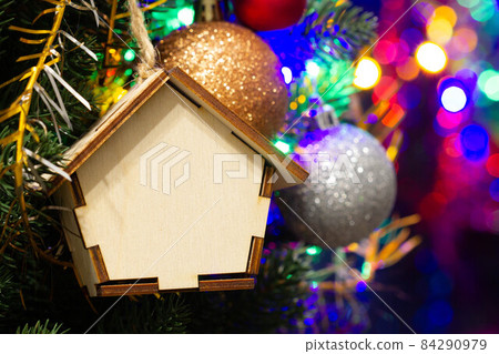 Christmas toy wooden house on the Christmas tree on the colorful lighting background. Beautiful Christmas decorations. Cool bright New Year's toys on the tree. Stunning Decorated Christmas Tree 84290979