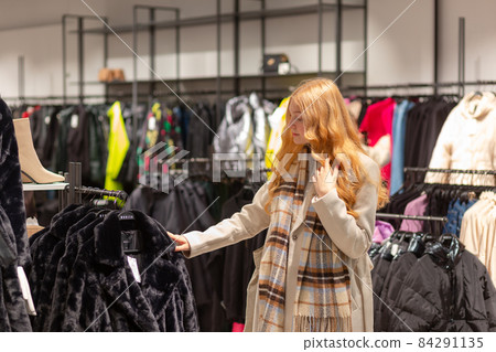 Young female customer with golden hair examining best fur coats 84291135