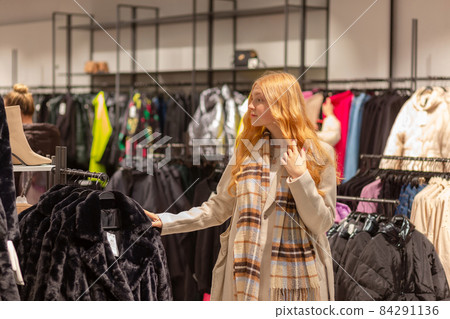 Young female customer with golden hair examining best fur coats Young female customer with golden hair examining best fur coats 84291136