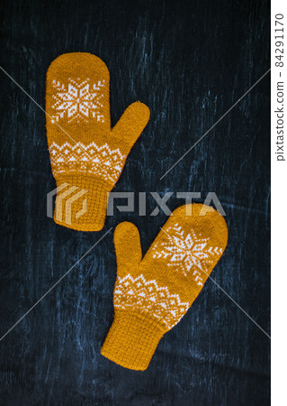 a pair of yellow orange knitted mittens on a dark blue-green-brown wooden a pair of yellow orange knitted mittens on a dark blue-green-brown wooden 84291170