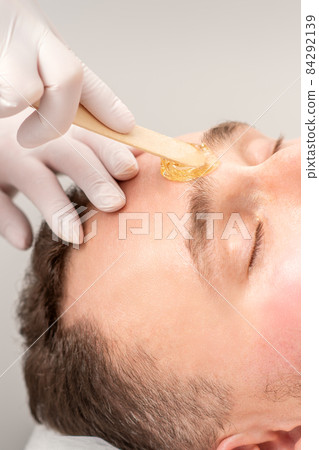 Beautician applying wax paste between eyebrows during the procedure of waxing in the beauty salon. 84292139