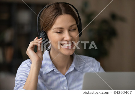 Woman wear wireless headset smile looks at laptop screen Woman wear wireless headset smile looks at laptop screen 84293407