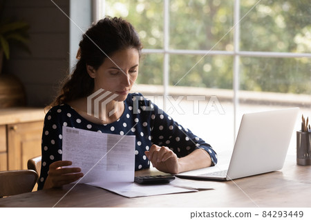Focused young latin female doing financial paperwork at home kitchen 84293449