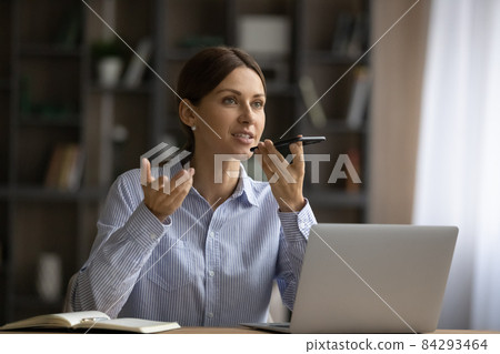 Attractive woman sit at desk holding smartphone talk on speakerphone Attractive woman sit at desk holding smartphone talk on speakerphone 84293464