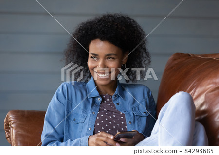 Dreamy smiling young African American woman using cellphone. Dreamy smiling young African American woman using cellphone. 84293685