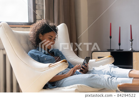 Happy pretty African girl resting in comfortable armchair Happy pretty African girl resting in comfortable armchair 84294522
