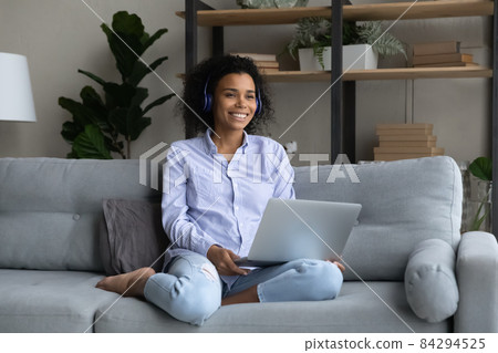 Smiling African American woman in wireless headphones looking in distance Smiling African American woman in wireless headphones looking in distance 84294525