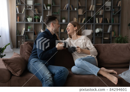 Happy couple chatting, holding cups of tea, relaxing on couch 84294601