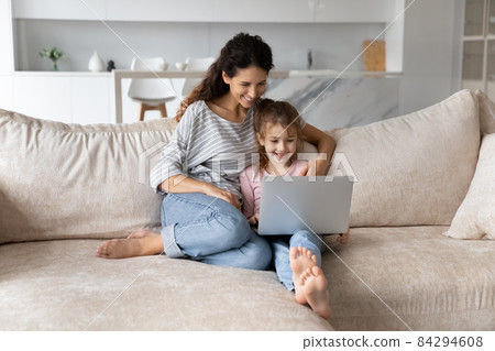 Smiling mother with adorable daughter using laptop sitting on couch Smiling mother with adorable daughter using laptop sitting on couch 84294608