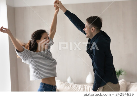 Cheery couple holding hands dancing at home Cheery couple holding hands dancing at home 84294639