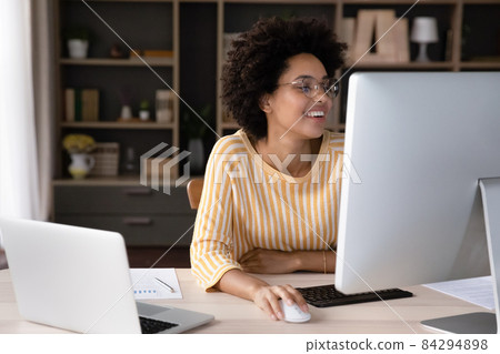 Happy female African business professional working at workstation monitor Happy female African business professional working at workstation monitor 84294898