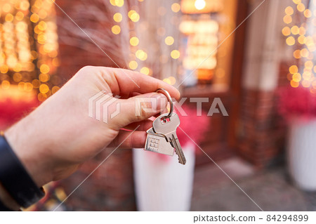 Rent a house for Christmas. Mortgage or rent concept. Man holding key with wooden house keychain . Real estate, hypothec, moving home or renting property. Christmas mood in blurred background. Rent a house for Christmas. Mortgage or rent concept. Man holding key with wooden house keychain . Real estate, hypothec, moving home or renting property. Christmas mood in blurred background. 84294899