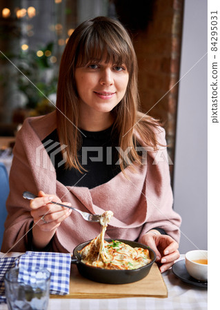 Potato with cheese casserole in a cast-iron frying pan. Close-up of a woman eating with a fork. Latvian cuisine 84295031