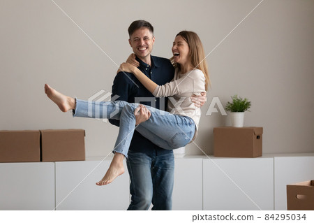 Overjoyed young husband lifting excited wife, family celebrating relocation 84295034