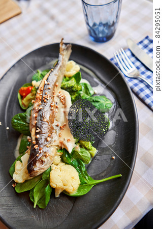 Roasted pike perch or cod fish with baked vegetables and spinach. Dish decorated with a slice of lemon. Restaurant menu 84295051