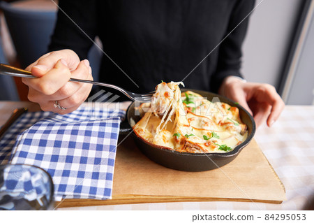 Potato with cheese casserole in a cast-iron frying pan. Close-up of a woman eating with a fork. Latvian cuisine 84295053