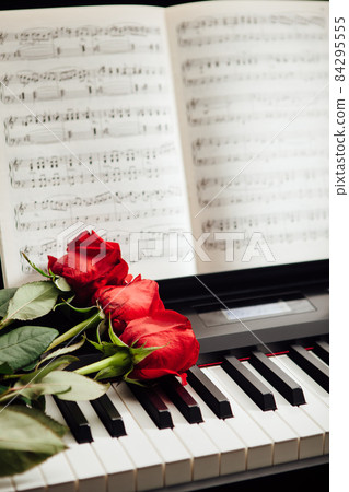 red roses on piano keys and music book 84295555