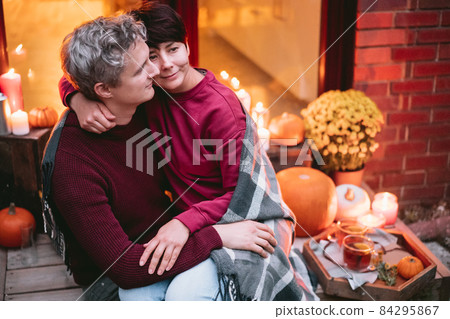 A couple having a romantic date on the porch of their home. Cozy ideas on how to spend time at home. Autumn tea time outdoors on house entrance decorated with pumpkins, flowers and burning candles 84295867