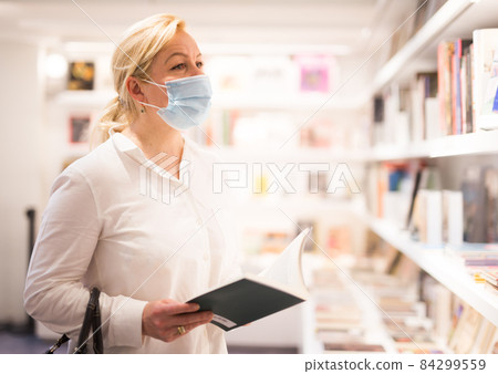 Mature woman in face mask looking at souvenir products 84299559