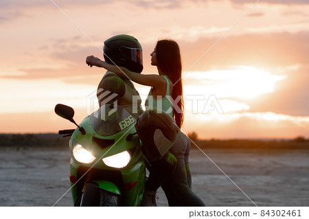 Couple embracing near motorbike on beach at sunset Couple embracing near motorbike on beach at sunset 84302461