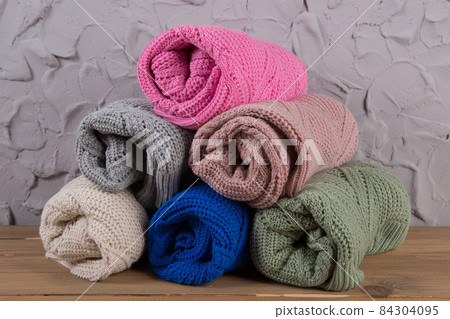 six colored woolen sweaters in rolls on the table, assortment of goods against the background of a concrete loft wall six colored woolen sweaters in rolls on the table, assortment of goods against the background of a concrete loft wall 84304095