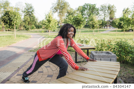an African-American girl is warming up near a park bench in the fresh air. 84304147