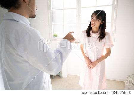 A nurse with a suspicious face being watched by a doctor 1 There is a copy space 84305608