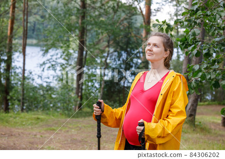 Pregnant woman walking in a summer forest using hiking poles 84306202