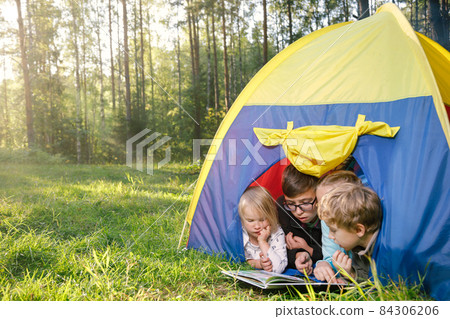 Children reading a book in a tent during summer holidays Children reading a book in a tent during summer holidays 84306206