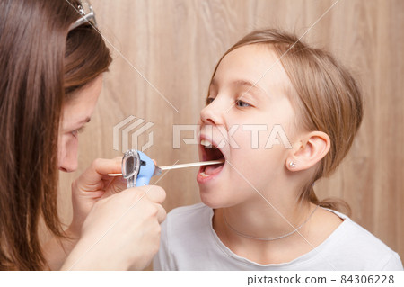 Child check up - doctor examining elementary age girl throat using wooden tongue depressor and torch Child check up - doctor examining elementary age girl throat using wooden tongue depressor and torch 84306228