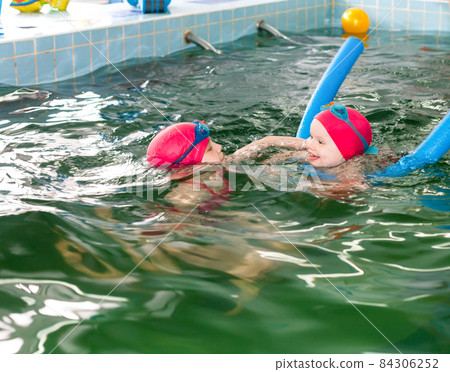 Girl teaching her little sister to swim in a pool 84306252