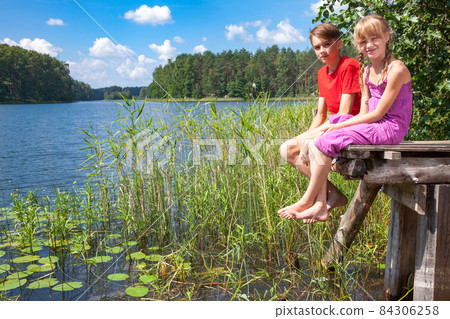 Children sitting on a pier by a summer lake Children sitting on a pier by a summer lake 84306258