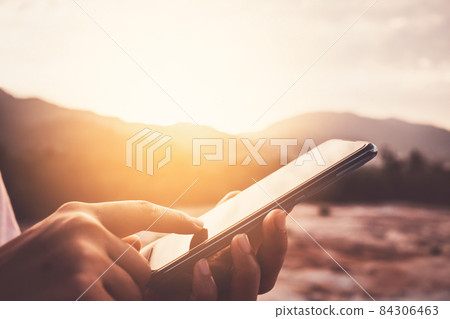 Woman hand using smart phone on top of mountain with sunset sky abstract background. Woman hand using smart phone on top of mountain with sunset sky abstract background. 84306463