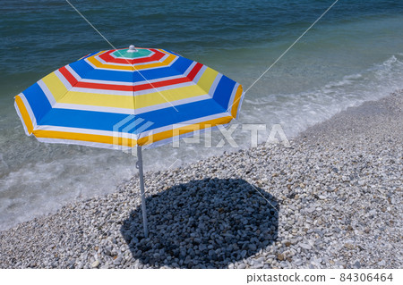 Empty stone beach with colorful sun umbrella Empty stone beach with colorful sun umbrella 84306464